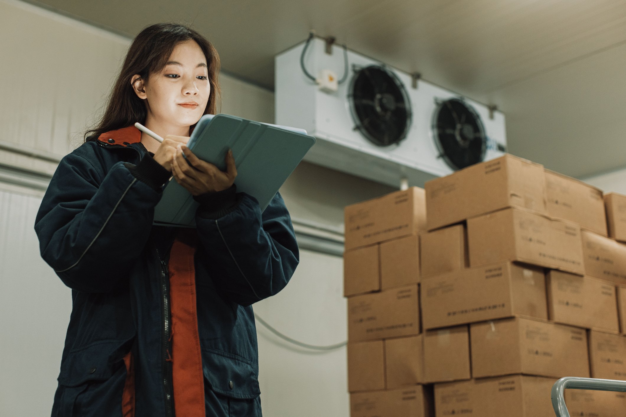 Cold storage worker woman using digital tablet to check stock.